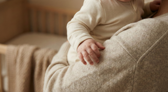 Overtired baby in mother’s arms during a night waking caused by a sleep regression, in a softly lit nursery